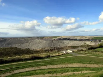 Northumberlandia’s vast sculpted earthworks rise beyond grassy slopes and dirt paths under a partly cloudy sky.