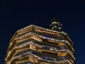 The Vessel lit up at night with golden lights and people gathered below.