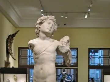 Incomplete marble statue of the Young Archer, showing a nude youthful male figure with curly hair and a diagonal band across the torso.