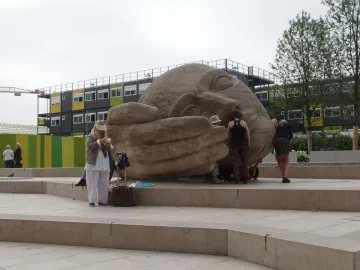 Écoute, a large stone sculpture of a reclining human head with a hand cupped near its ear, in a Paris plaza.