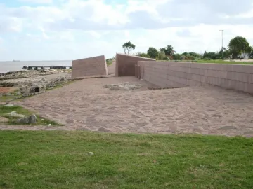 Holocaust Memorial with light pink granite walls beside a rocky shoreline and water.
