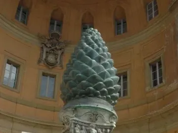 La Pigna, a large green pine cone sculpture on an ornate stone pedestal in front of a curved building.