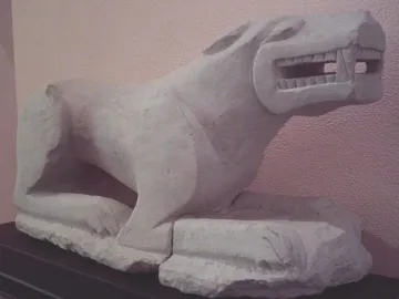 Leona de Baena stone lioness sculpture on a dark base against a pale wall.
