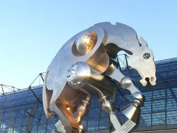 Rolling Horse sculpture in front of a modern glass building under a clear blue sky.
