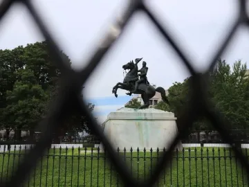 Andrew Jackson statue on a rearing horse, seen through a blurred fence with trees and buildings in the background.