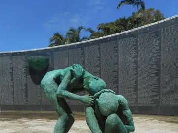 Bronze figures at the Holocaust Memorial beside a curved wall covered with inscriptions.