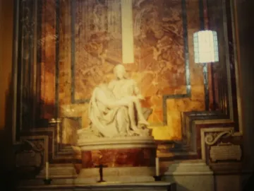 Michelangelo\'s Pietà in white marble, with the draped Virgin Mary holding Christ across her lap inside a patterned church interior.