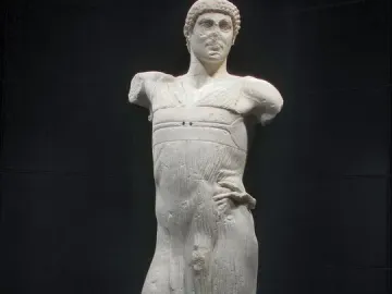 The Motya Charioteer, a white marble male statue missing its arms, shown against a dark background.