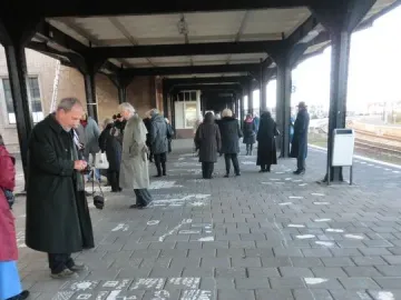 People stand on a covered train platform beside chalk drawings and symbols spread across the paving stones.