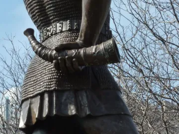 Close-up of Leif, the Discoverer showing bronze chainmail armor and an ornate horn-shaped object in his hand.