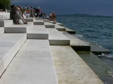 Concrete steps of the Sea Organ descending into a dark, choppy sea, with people seated on the upper levels.