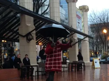 Allow Me sculpture of a figure in a checkered coat holding an open umbrella on a wet brick plaza.
