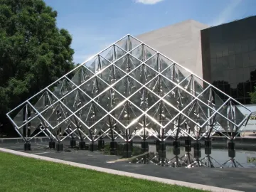 Delta Solar sculpture with reflective triangular panels rising above a dark pool of water.