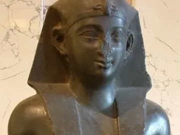 Fragmentary bust of a Ptolemaic king with an Egyptian nemes headcloth, broad collar, and broken nose.