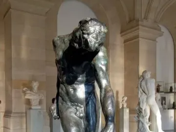 The Shade, a dark bronze male figure standing with bowed head in a museum hall.