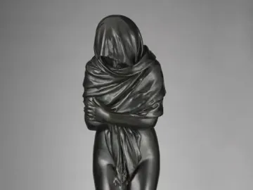 Winter bronze sculpture of a draped figure standing with arms crossed on a circular base.