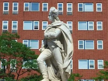 George Washington statue on a tiered pedestal in front of a brick building, with trees on either side.