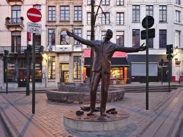 L\'Envol bronze sculpture of a man in a suit singing into a microphone with his arms outstretched in a cobblestone square.