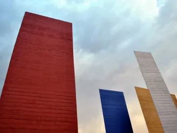 Torres de Satélite geometric towers in red, blue, gray, and gold against a cloudy sky.