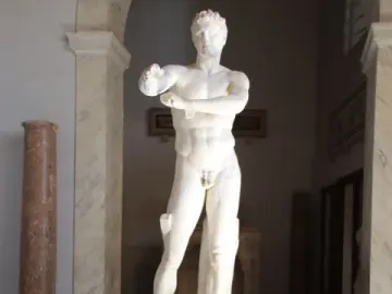 Apoxyomenos, a full-length marble statue of a nude male figure with his arms bent across his chest in a museum gallery.