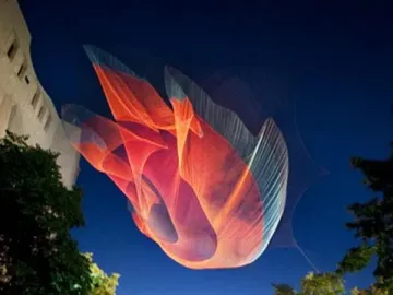 An enormous colorful textile installation floats above a city street at dusk.