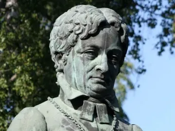 Weathered green statue of Frans Michael Franzén in clerical vestments with a crucifix necklace.