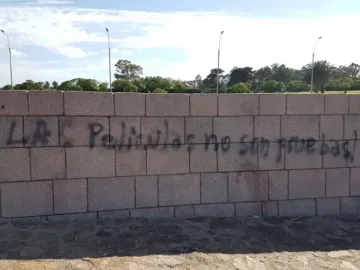 Graffiti on a stone wall at the Holocaust Memorial, with trees and streetlights visible above it.