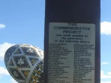The Vegreville egg sculpture stands in the background with a commemorative plaque in the foreground on grass.