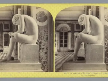 The Boy with Thorn statue, a nude boy seated on a pedestal and bent over his foot in an ornate interior.
