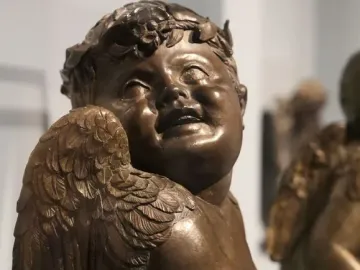 Close-up of Donatello’s bronze candelabra angel with a leafy wreath, feathered wings, and an open mouth.