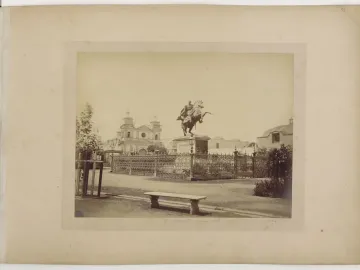 The Equestrian Statue of Simón Bolívar stands on a tall pedestal in a fenced plaza with a church and twin bell towers behind it.