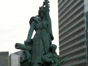 La Défense de Paris bronze monument with a crowned female figure, standard, cannon, and seated soldier in front of modern buildings
