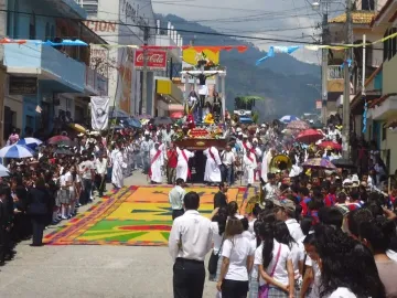A religious procession float with San Juan Patrón and a crucified figure surrounded by flowers.