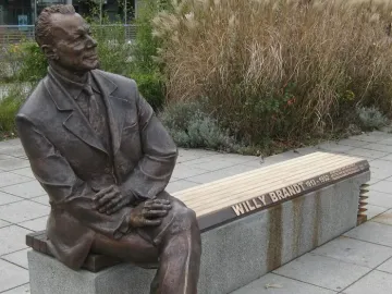 Willy Brandt Memorial bronze statue of a seated man in a suit on a bench, with tall dry grasses behind it.