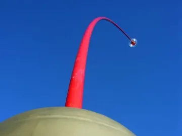 Wind Wand sculpture with a crimson rod rising from a rounded dome against a blue sky.