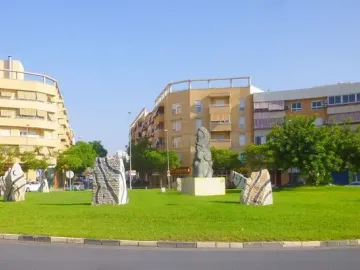 Dona Lluna sculpture with a crescent moon on its head standing on a pedestal in a grassy roundabout