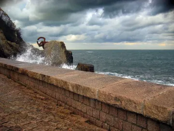 Peine del Viento sculpture beside rocky cliffs as a wave crashes into the rust-colored metal forms.