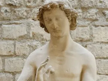 Adam stone sculpture with a raised left hand and fig leaves covering the lower body