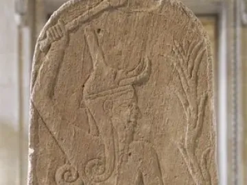 Baal with Thunderbolt carved on a weathered stone stele, shown with a horned figure holding a club and a stylized plant-like shaft beside a smaller figure.