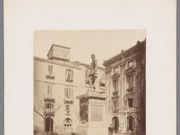 The John of Austria monument stands on an ornate pedestal in a public square, surrounded by a low decorative fence and garden.