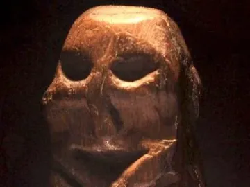 Mannetje van Willemstad wooden statuette with deep eye hollows and a recessed mouth on a transparent base.
