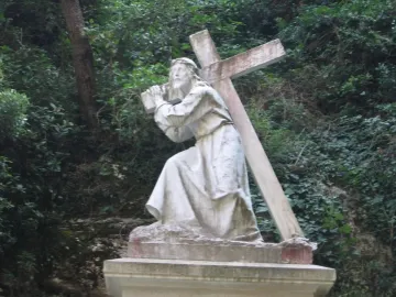 Monumental Rosary of Montserrat sculpture of Jesus carrying a cross beside dense greenery