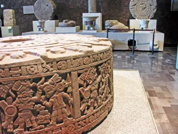 Stone of Motecuhzoma I, a large round stone monolith with carved figures and symbolic reliefs displayed in a museum setting.