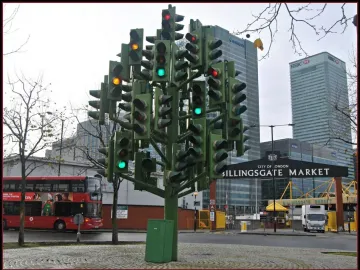 The Traffic Light Tree sculpture made from green traffic light poles, with illuminated red, amber, and green signals in an urban street setting.