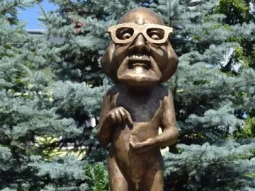 Citizen Włapko bronze statue of a male figure with a caricatured head, glasses, and a wide grin on a white pedestal.