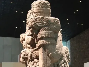 Coatlicue stone sculpture with serpent motifs, skull-like necklace details, and a textured skirt.