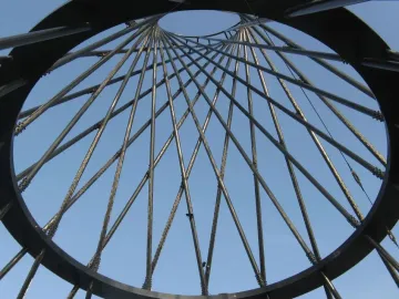 Upward view through Mae West’s metal ring and lattice of converging rods against a blue sky.