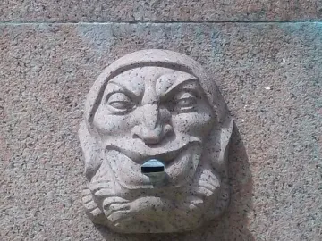 Carved stone face with a wide smile and metal spout on the Obelisk of Montevideo.