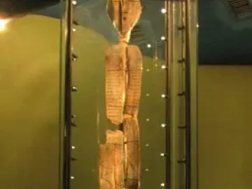 The Shigir Idol stands upright in a glass case, showing an oval head and carved geometric patterns on its weathered wooden surface.