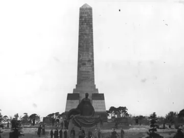 The Soviet War Memorial Schönholzer Heide with a tall stone obelisk and seated statue, surrounded by people on the steps.